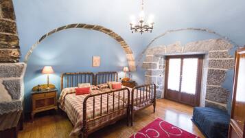 A bedroom with a wooden bed, two bedside tables with lamps, a red rug, and stone walls.