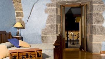 Una habitación con cama, una mesita de noche de madera con lámpara, una maleta y una pared de piedra.