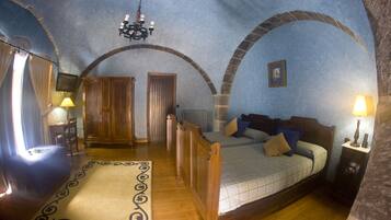 A bedroom with a wooden bed, a nightstand, a lamp, and a view of the outside through an arched window.