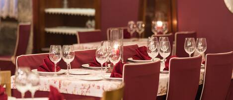 A dining table set with multiple wine glasses and plates, surrounded by red upholstered chairs.