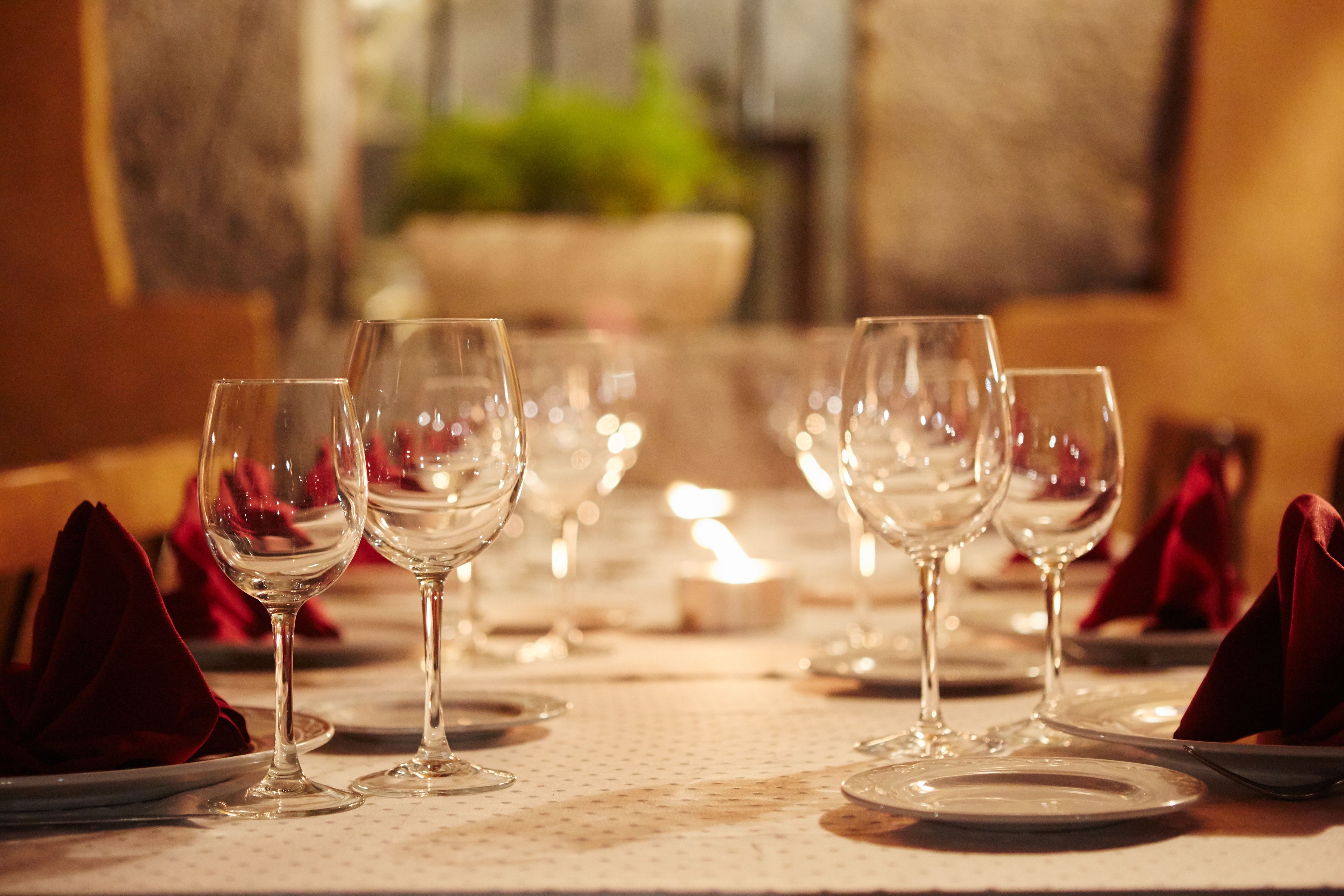 Una mesa de comedor dispuesta con varias copas de vino y platos, con servilletas rojas dobladas sobre la mesa.