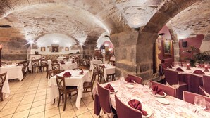 Un restaurant doté d’arches en pierre, de tables recouvertes de nappes blanches et agrémentées de serviettes rouges, et d’un sol carrelé.