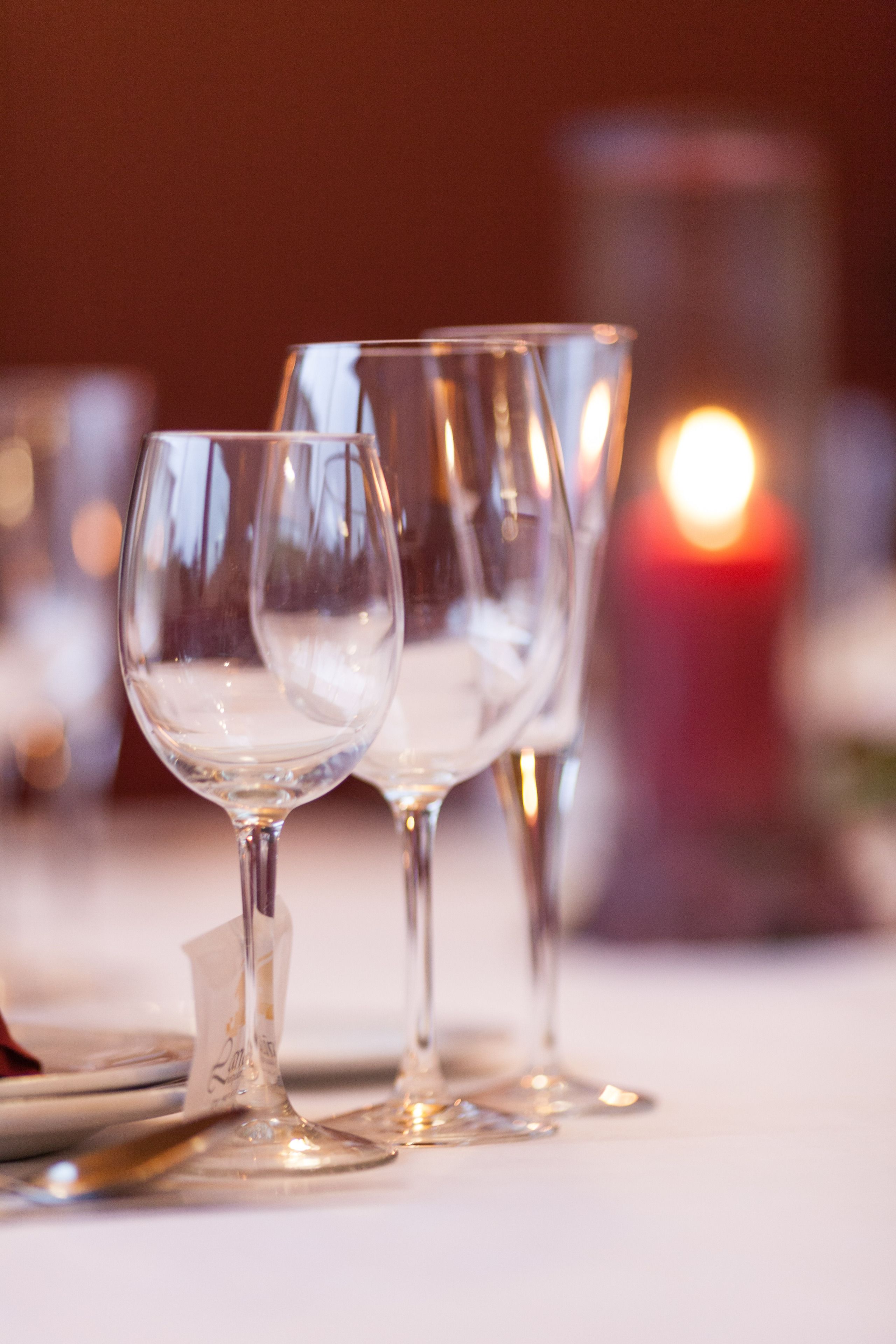 A close-up of three empty wine glasses on a table with a lit candle in the background.