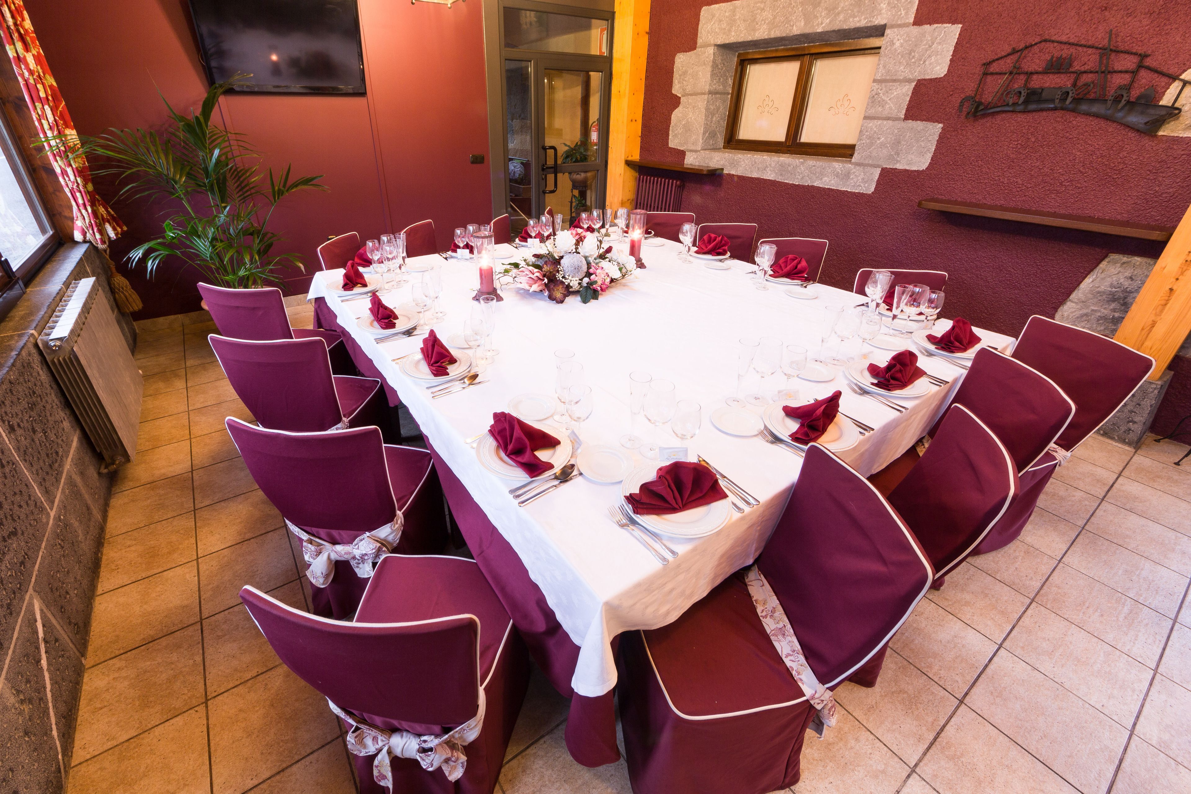 Mesa de comedor dispuesta para un evento formal, con manteles blancos, servilletas rojas y sillas a juego.