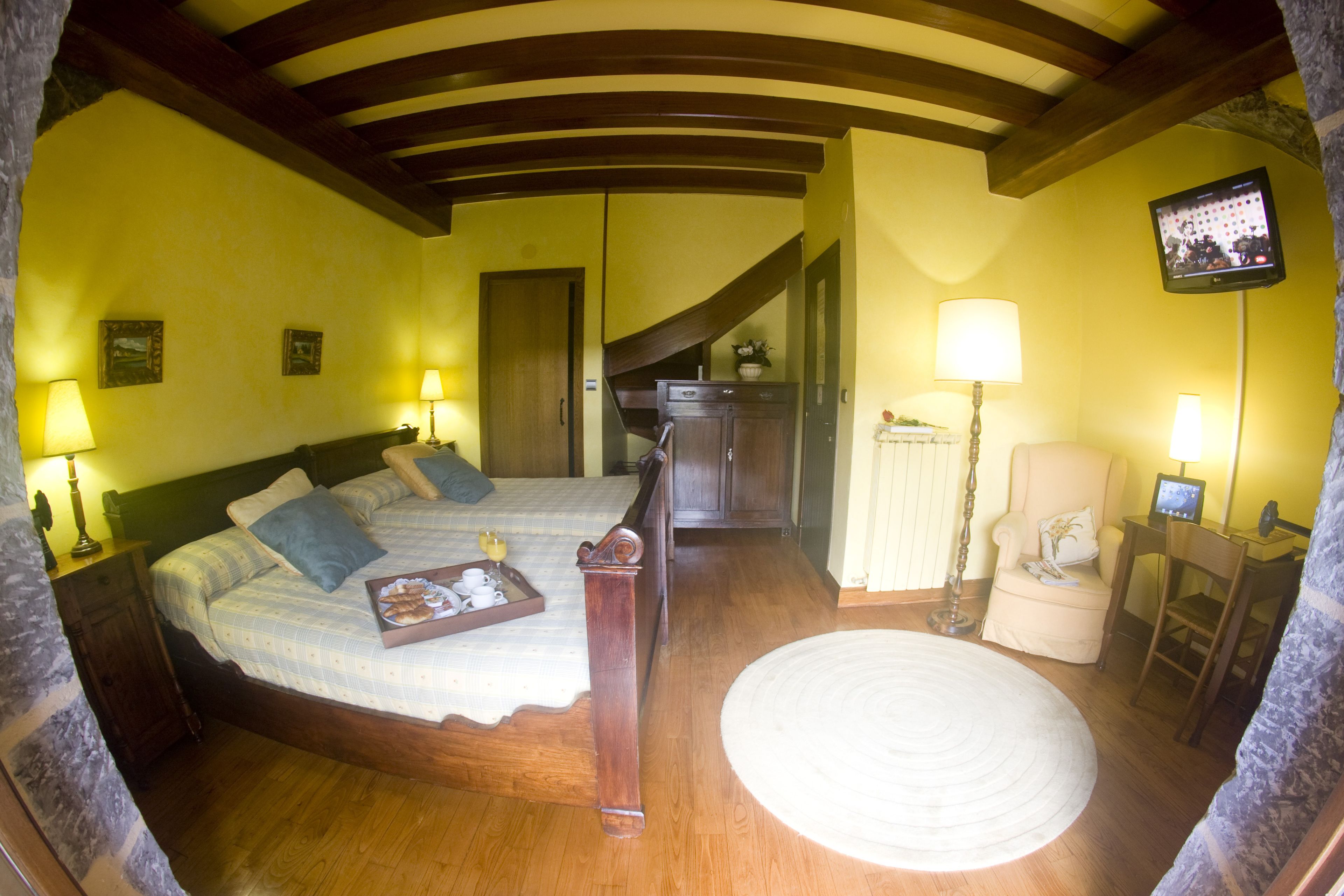Un dormitorio con una cama grande, cabecera de madera, mesita de noche, lámpara, silla, escritorio, televisor y un mueble pequeño.