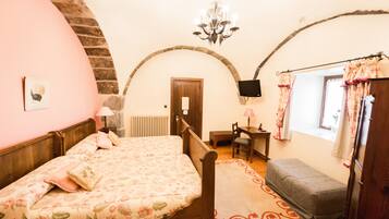 A bedroom with a bed, a bench, a desk, a chair, a television, and a window with curtains.