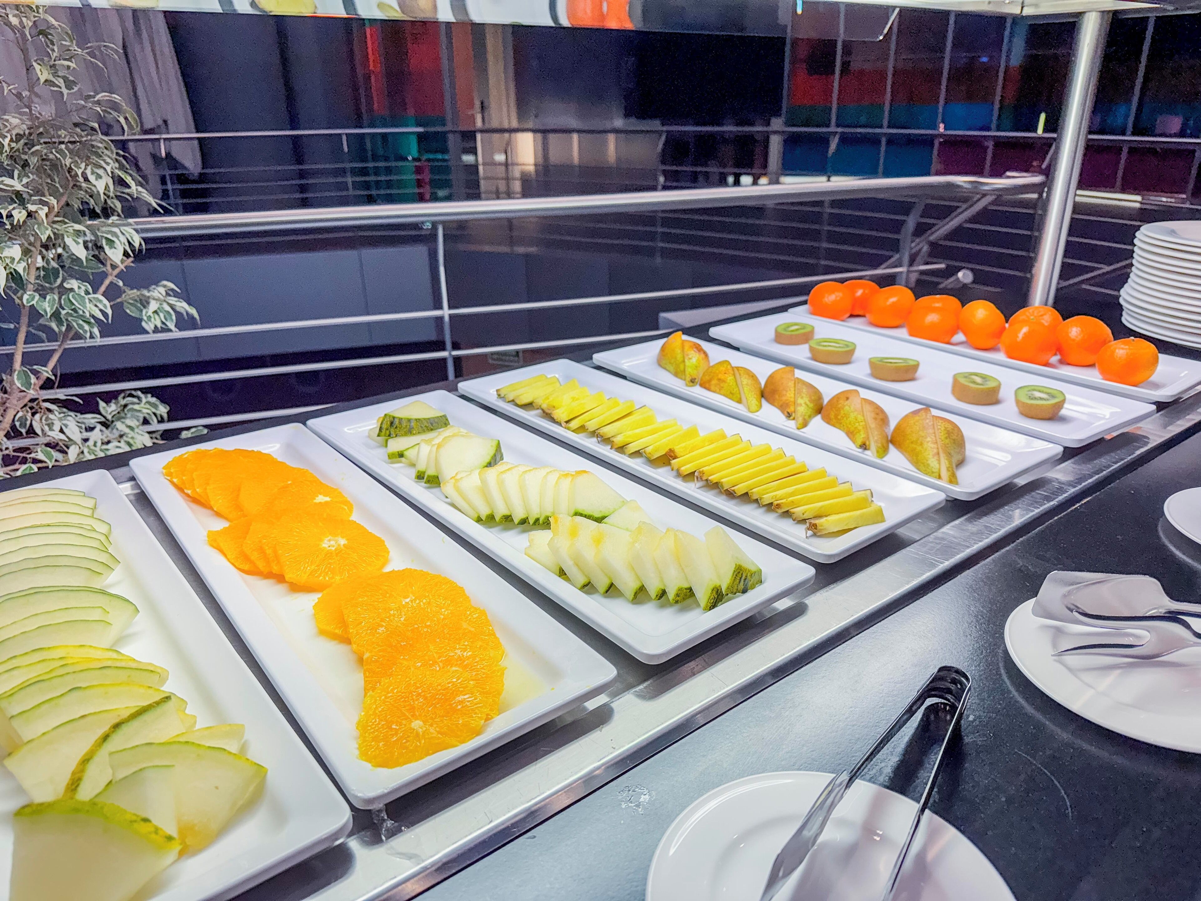 A buffet with various fruits and vegetables arranged on white trays.