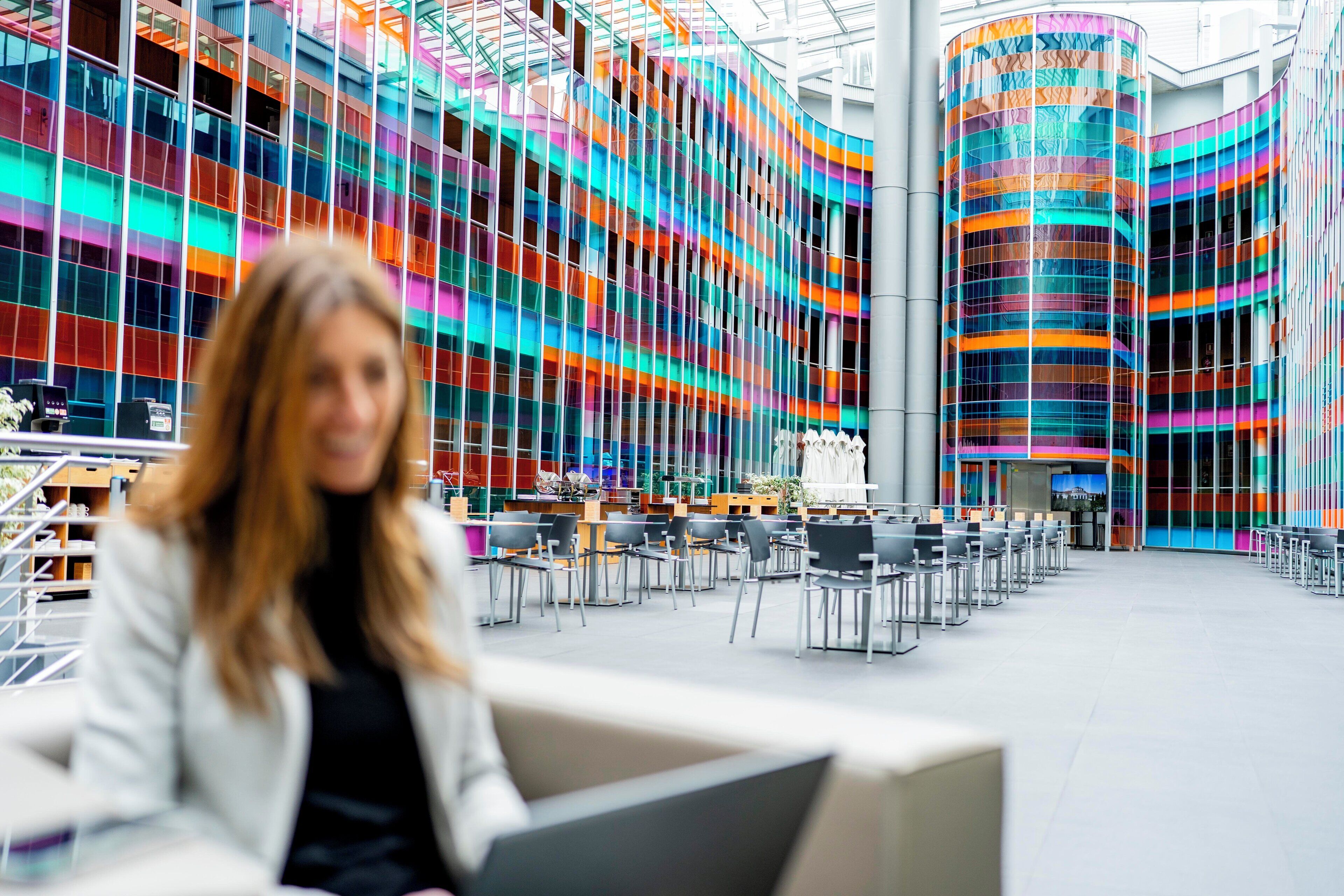 Un edificio moderno con una fachada vibrante y de varios colores, y un interior espacioso con numerosas sillas y mesas.