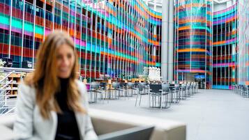 Un edificio moderno con una fachada vibrante y de varios colores, y un interior espacioso con numerosas sillas y mesas.