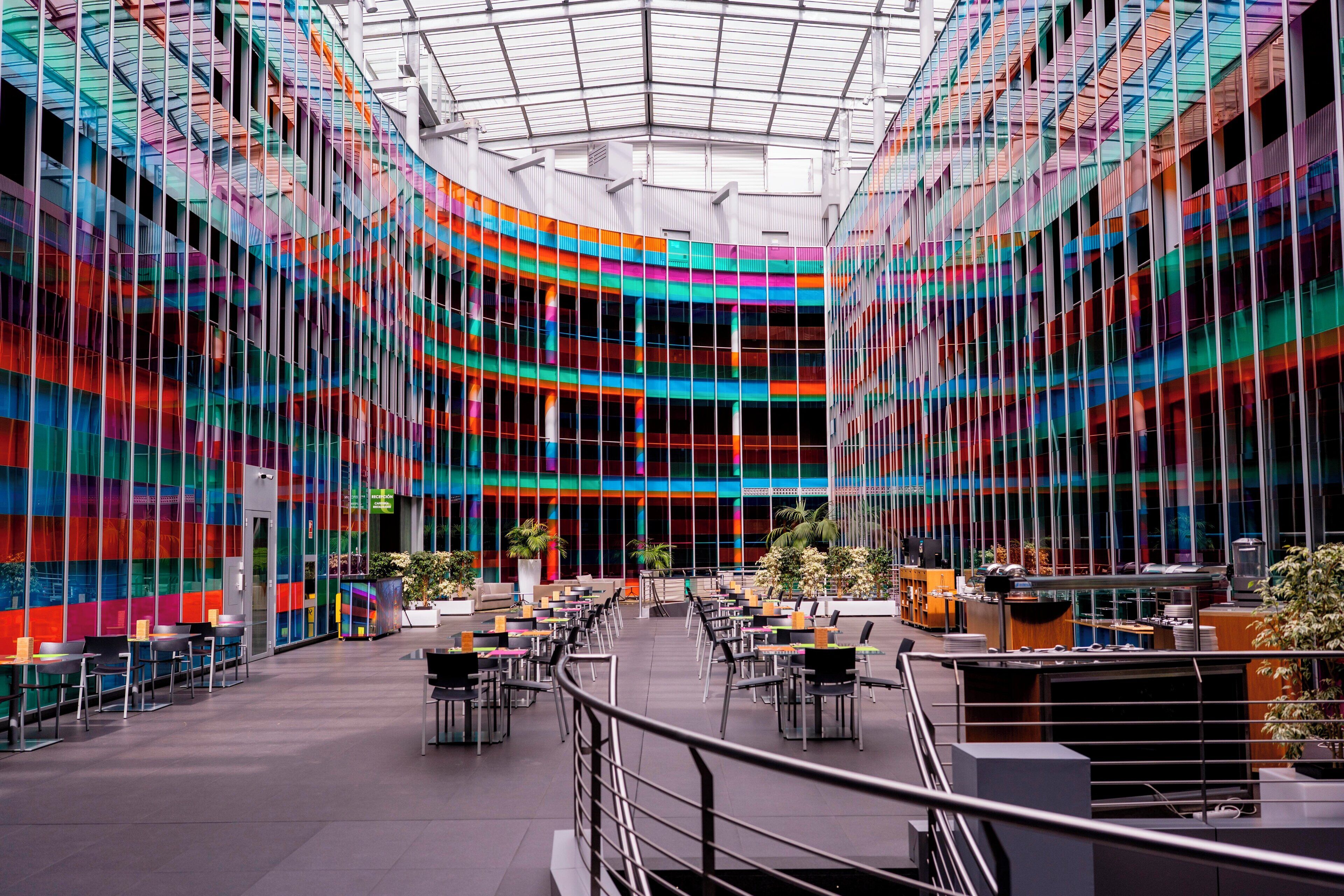 Un atrium moderne avec un toit de verre, plusieurs niveaux d’assises et des plantes d’intérieur.