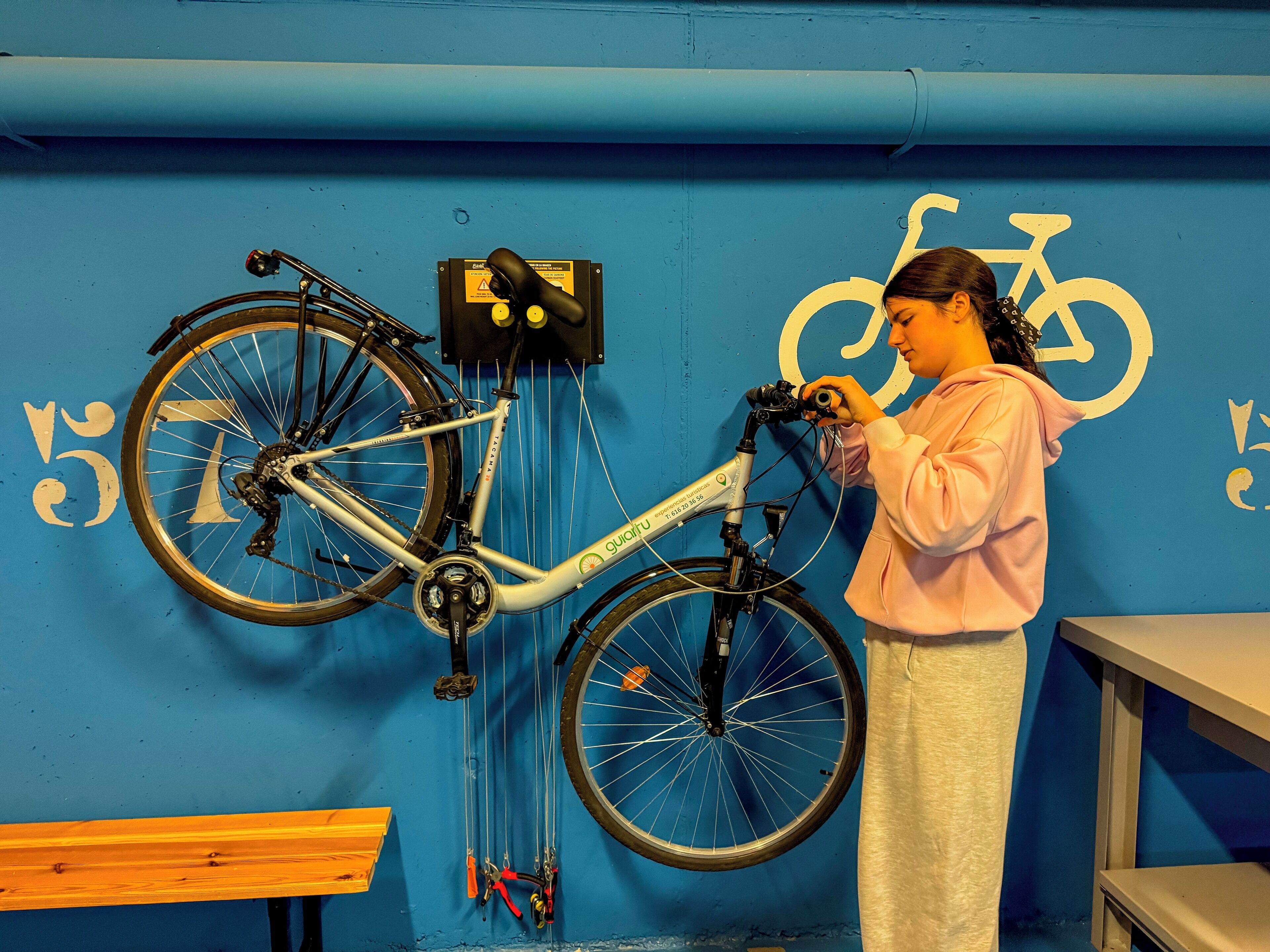 Eine Person justiert ein Fahrrad in einem Raum mit blauen Wänden, einem Fahrradsymbol und einer Kontaktnummer.
