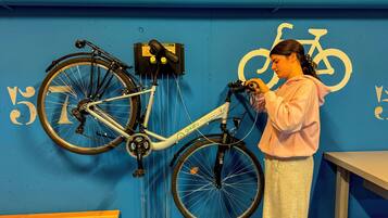 Eine Person justiert ein Fahrrad in einem Raum mit blauen Wänden, einem Fahrradsymbol und einer Kontaktnummer.