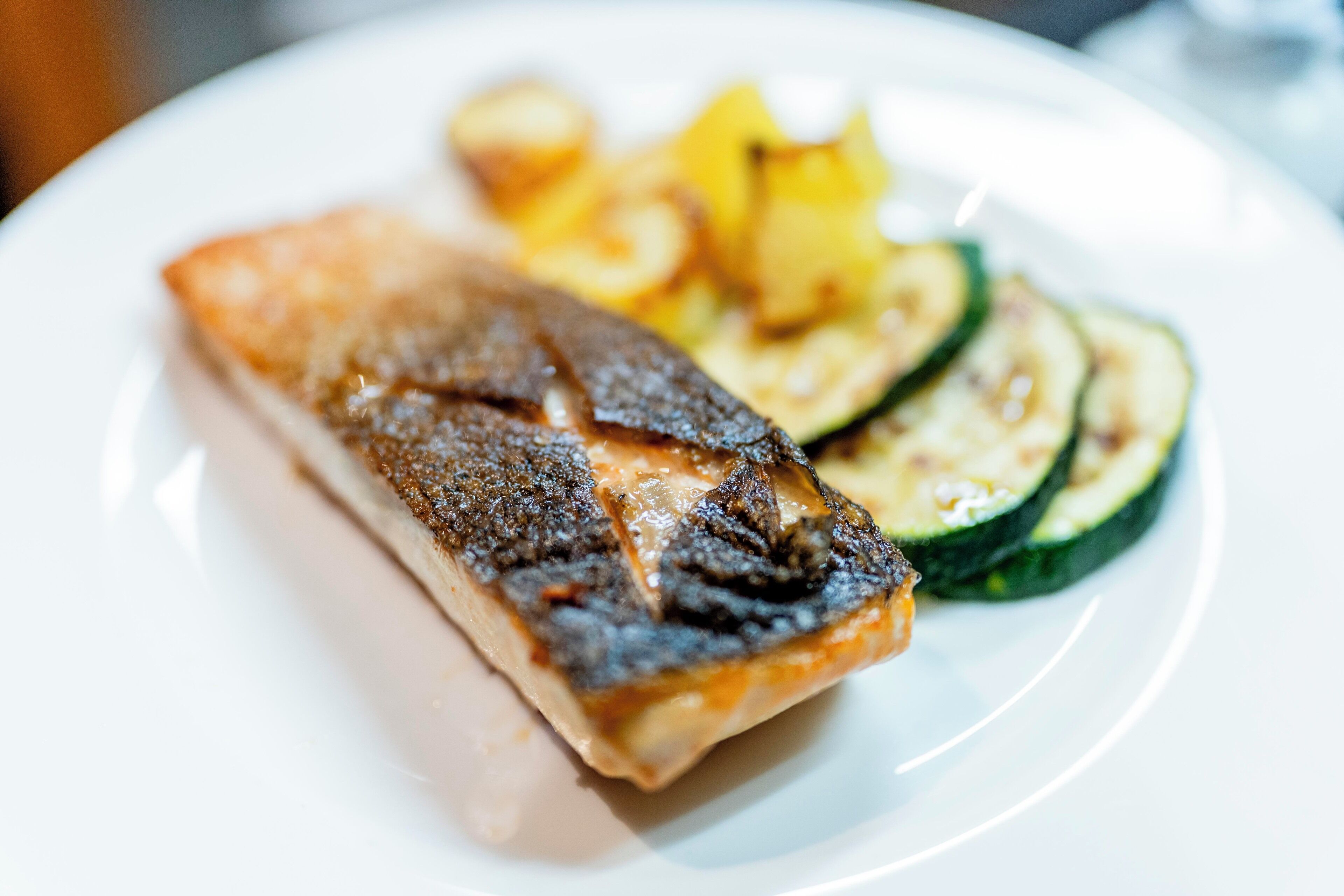 A plate with grilled fish, zucchini slices, and roasted potatoes.