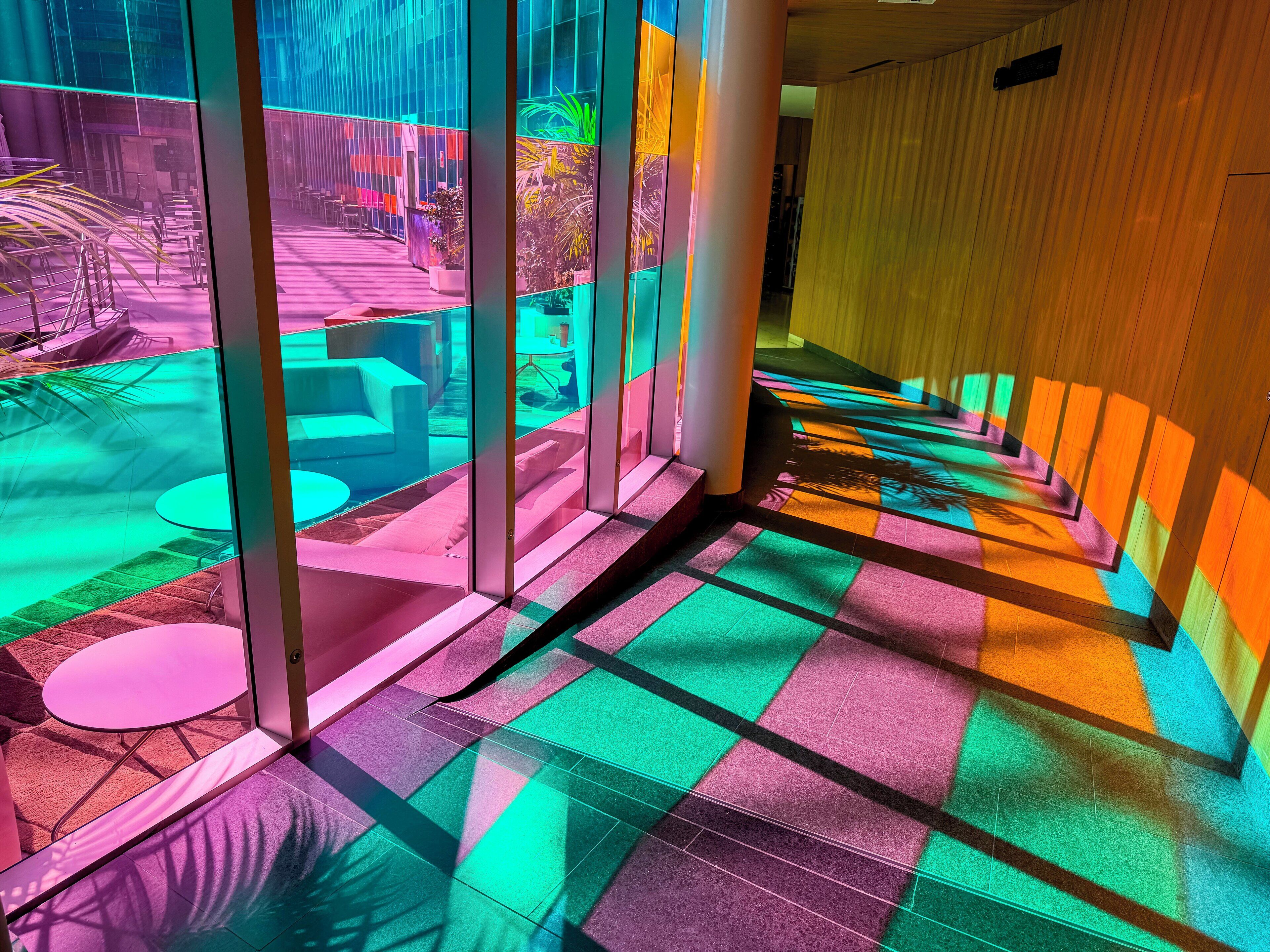 Un espace intérieur moderne avec des murs en verre, un sol carrelé et un coin salon équipé de tables et de chaises.