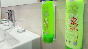 A bathroom with a white sink, a chrome faucet, and two green bottles of ECO hand and body lotion.