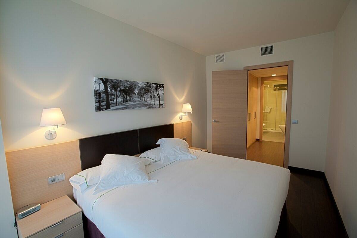 A hotel room with a bed, bedside lamps, a nightstand, a wall-mounted picture, and a door leading to a bathroom.