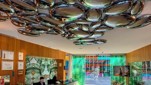 Un moderno vestíbulo de hotel con techo reflectante, una recepción y un mural de colores.