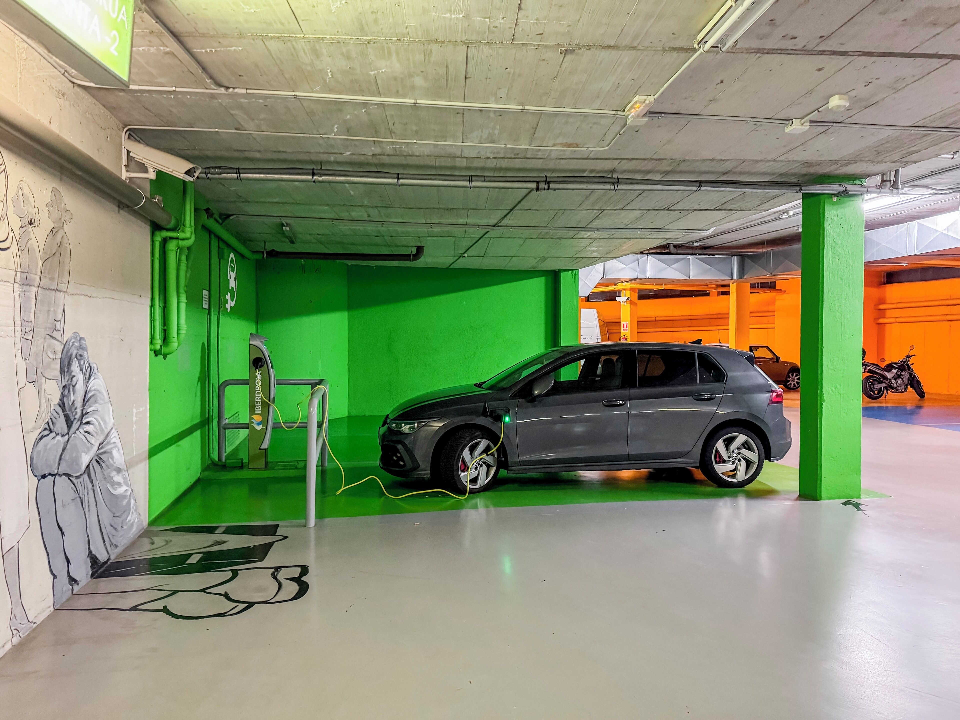 Eine Tiefgarage mit grüner Wand, Wandgemälde und einer Ladestation.