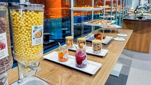 Un bufé con diversas opciones de comida y bebidas, incluyendo alternativas sin gluten, en un espacio moderno con divisiones de vidrio.