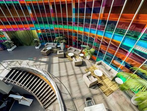 A modern atrium with a central seating area, a staircase, and a glass wall with colorful reflections. - Jardines de Uleta Suites (Vitoria-Gasteiz)