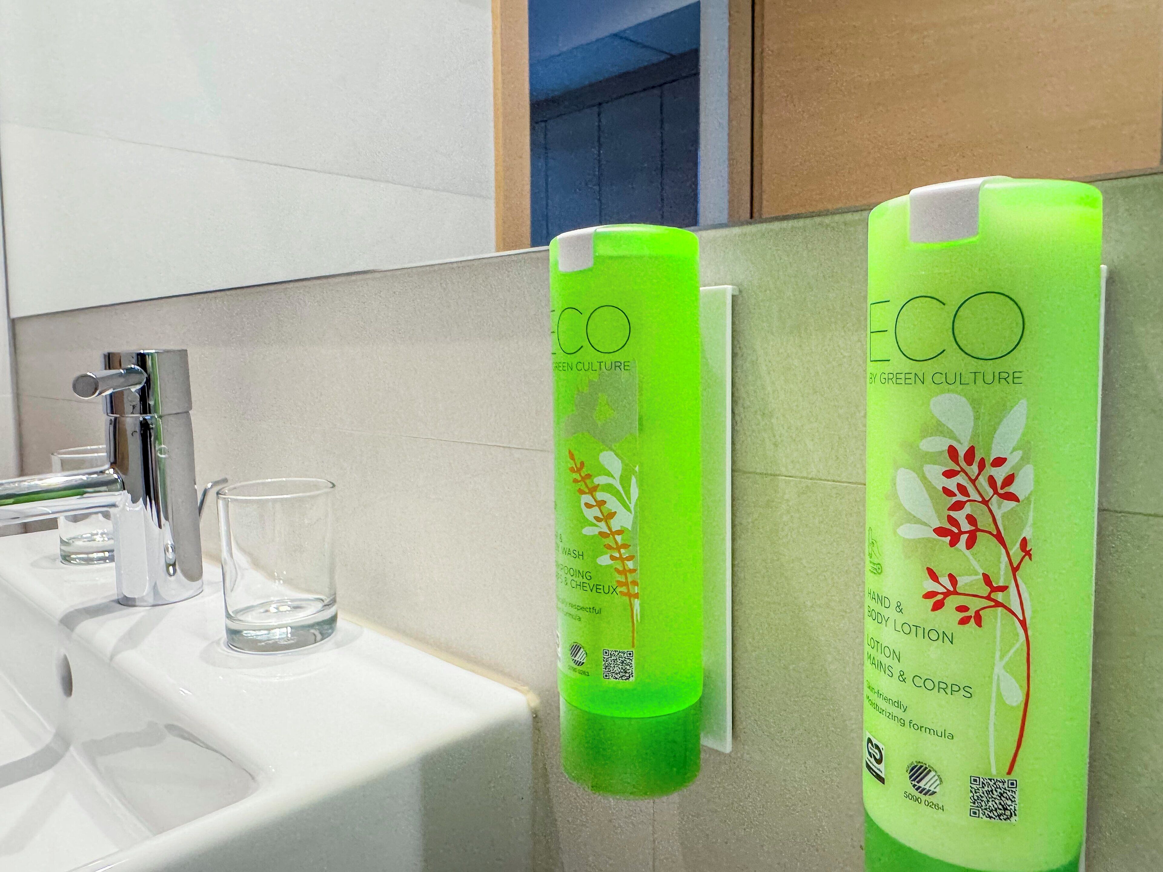 Une salle de bain avec un lavabo blanc, un robinet chromé et deux flacons verts de lotion pour les mains et le corps de la marque ECO.