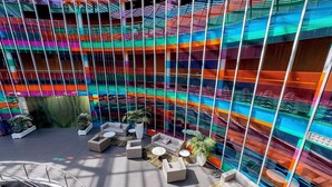 Un atrio moderno con fachada de vidrio colorida, zonas de estar y una escalera.