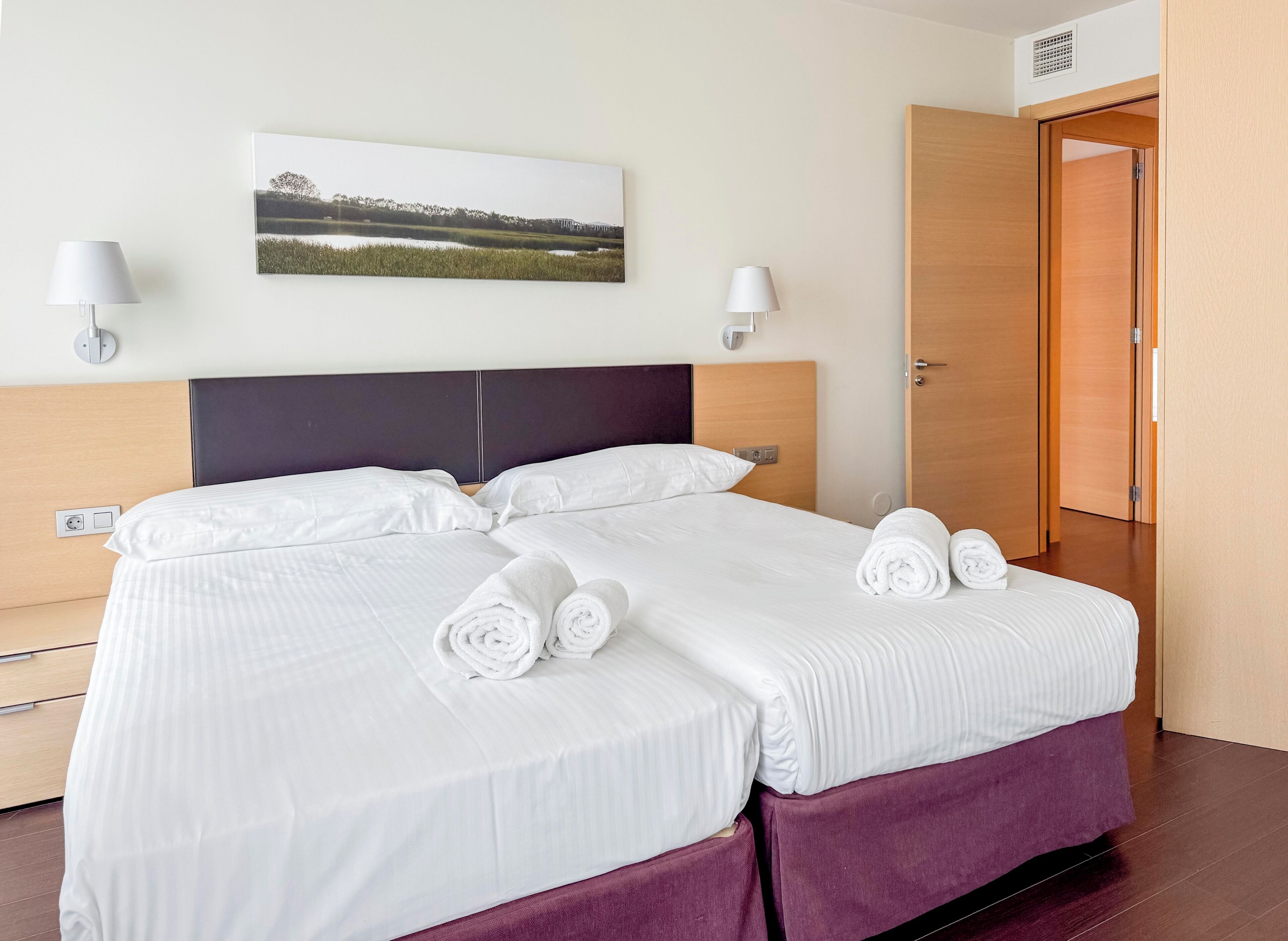 A hotel room with a bed, two wall-mounted lamps, a picture on the wall, and a wooden door.