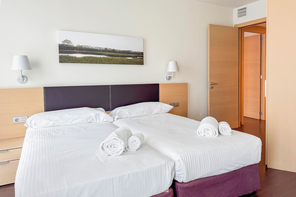 A hotel room with a bed, two wall-mounted lamps, a picture on the wall, and a wooden door.