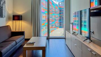 Habitación de hotel moderna con sofá, una mesa de centro, televisor y vistas a edificios de vidrio de colores.