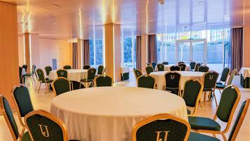 A conference room with round tables and chairs, large windows, and a modern ceiling design.