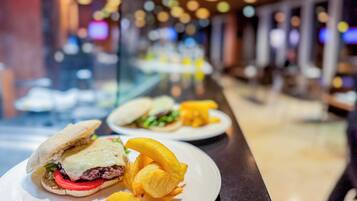 Un restaurante con una barra larga, comidas como sándwiches y papas fritas, y un fondo desenfocado con luces.