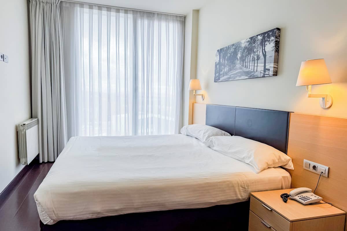 A hotel room with a bed, bedside lamps, a painting, and a phone on the nightstand.