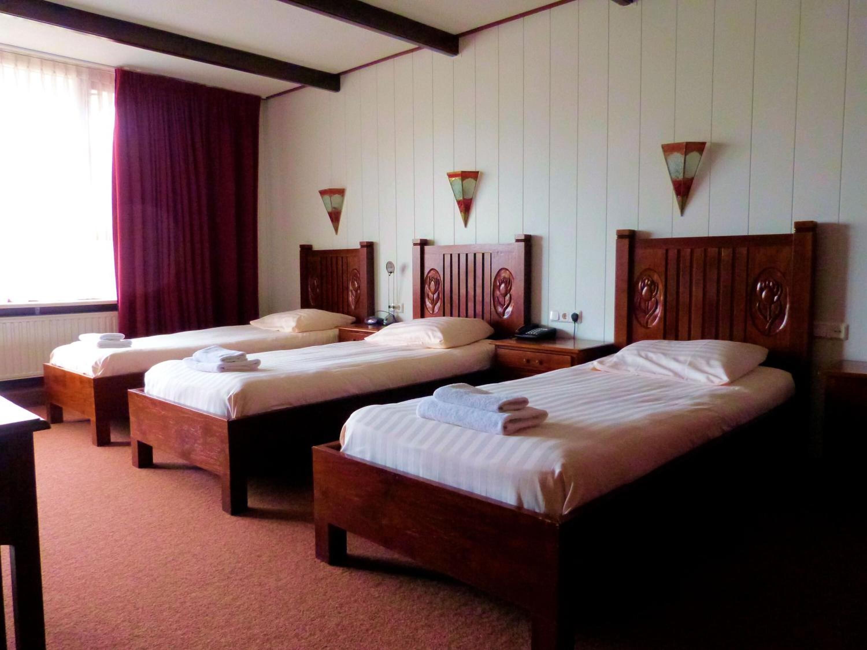 Una camera d'albergo con tre letti di legno, ognuno con un poggiatesta in legno e un comodino.
