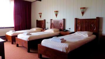 Una camera d'albergo con tre letti di legno, ognuno con un poggiatesta in legno e un comodino.
