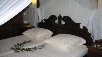 A bed with white linens, a wooden headboard, and a bedside table with a plate of food.