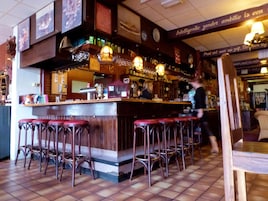 Una zona de bar con taburetes, una barra y diversas botellas y vasos.