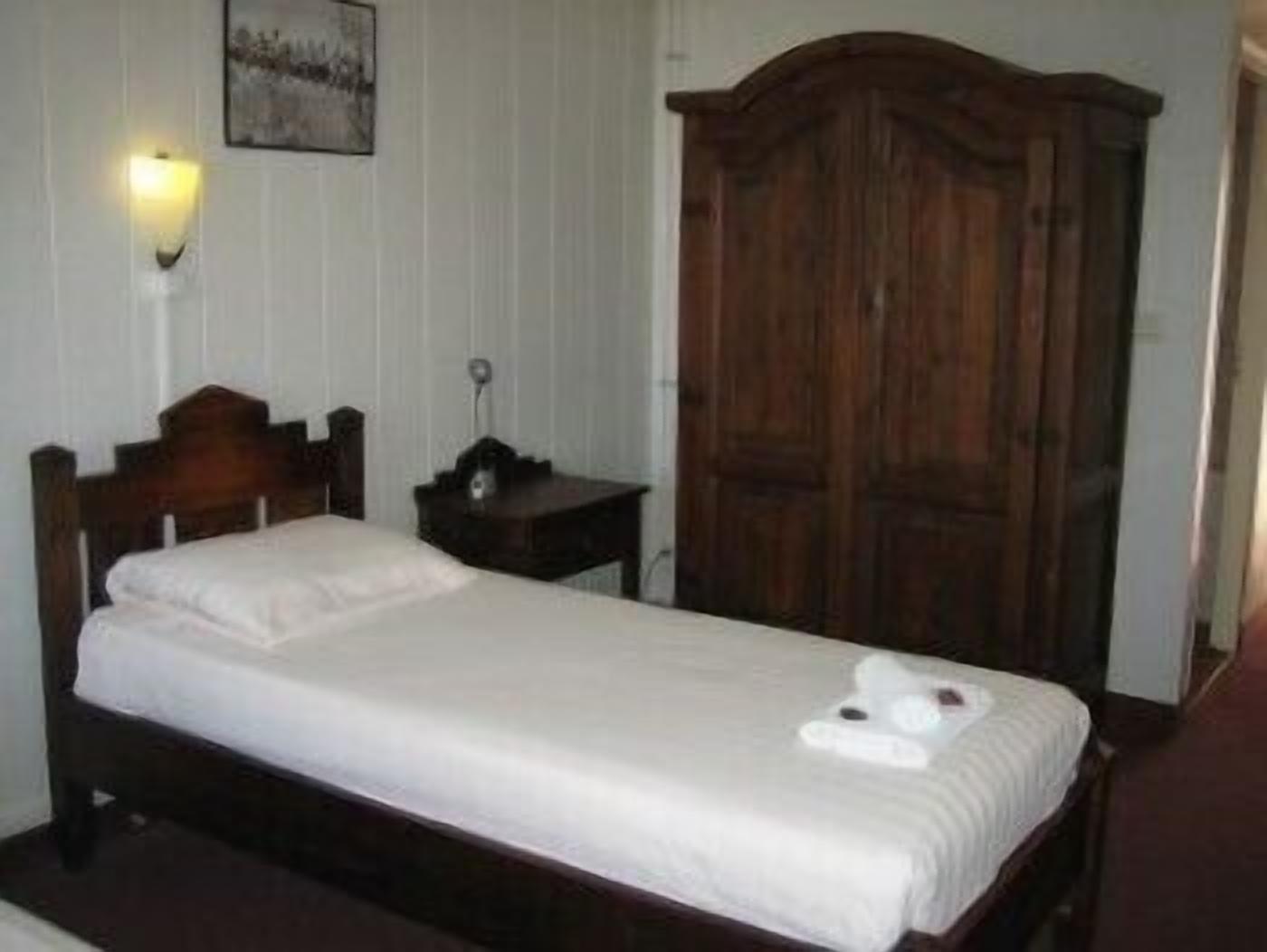 A single bed with a wooden headboard, a bedside table with a lamp, and a wardrobe.