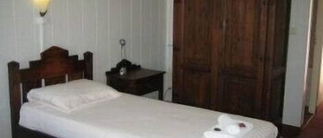 A single bed with a wooden headboard, a bedside table with a lamp, and a wardrobe.