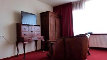 Quarto de hotel com um armário de madeira, televisão por cima, tapete vermelho e uma janela com cortinas.