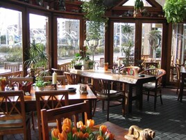 Un restaurante con mobiliario de madera, ventanas amplias y plantas de interior.