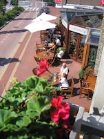 Un área de estar al aire libre con mesas y sillas, un letrero que indica una cafetería y vista de la calle.