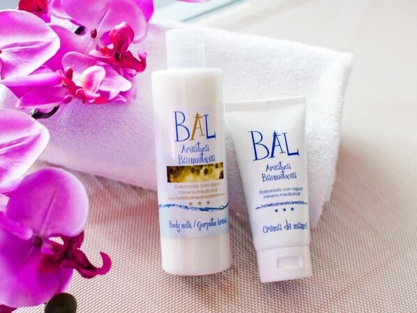 Zwei Flaschen BAL Körperlotion und eine Tube BAL Körpercreme liegen auf einem weißen Handtuch, im Hintergrund befinden sich rosa Blumen.