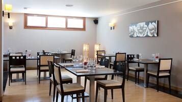 A dining area with multiple tables and chairs, equipped with wine glasses and water glasses.