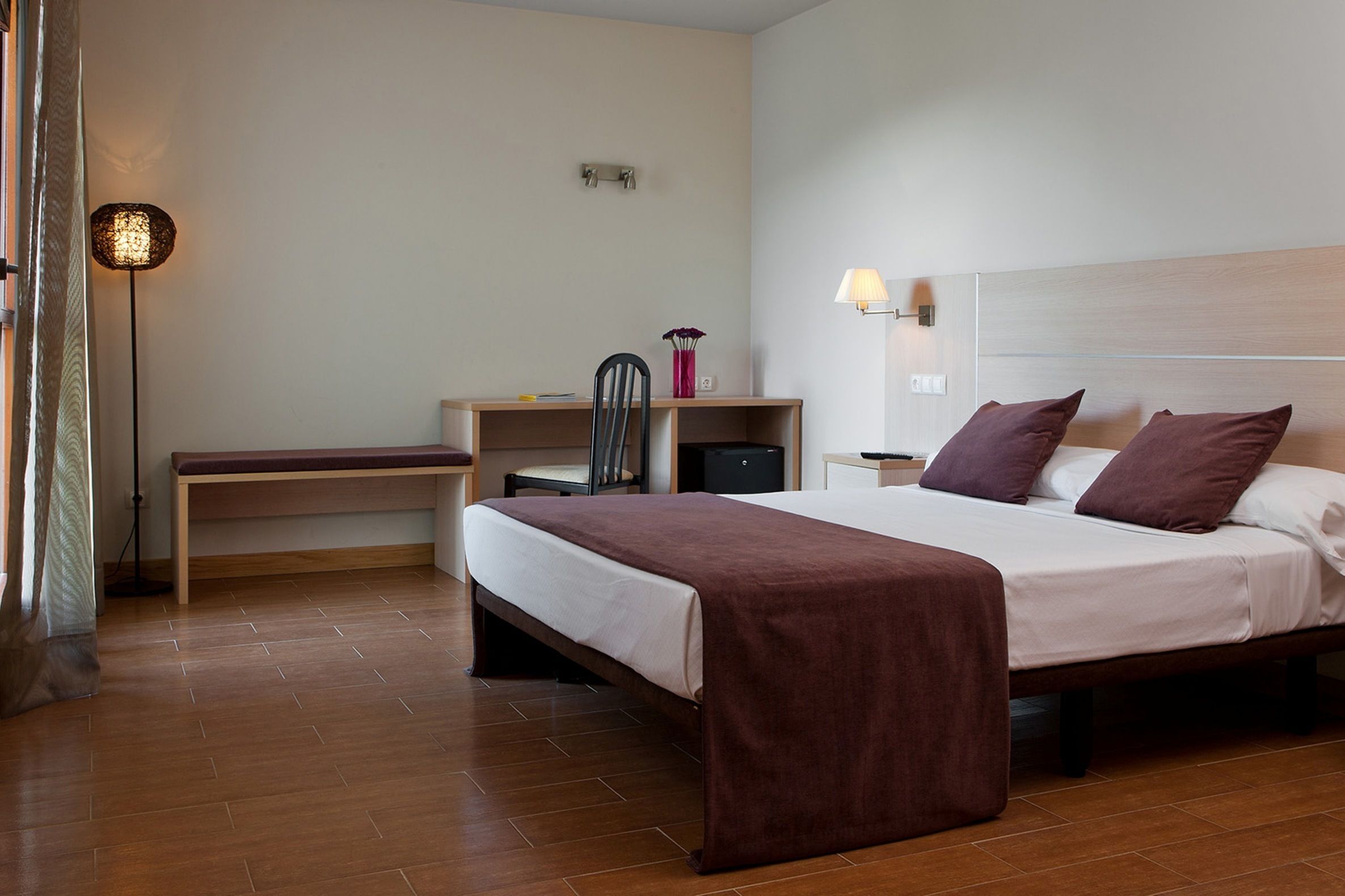 Une chambre d’hôtel comprenant un lit, un bureau, une chaise, une lampe et une table de chevet.