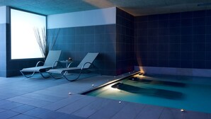 A modern indoor pool area with two lounge chairs, a small table, and a wall-mounted plant. - Hotel Balneario Areatza (Areatza)