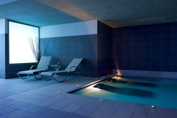 A modern indoor pool area with two lounge chairs, a small table, and a wall-mounted plant.