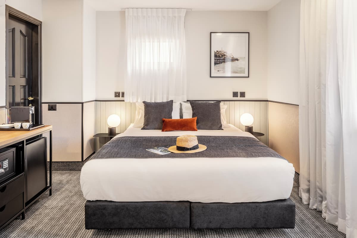 A hotel room with a large bed, bedside tables, a desk, and a wardrobe.