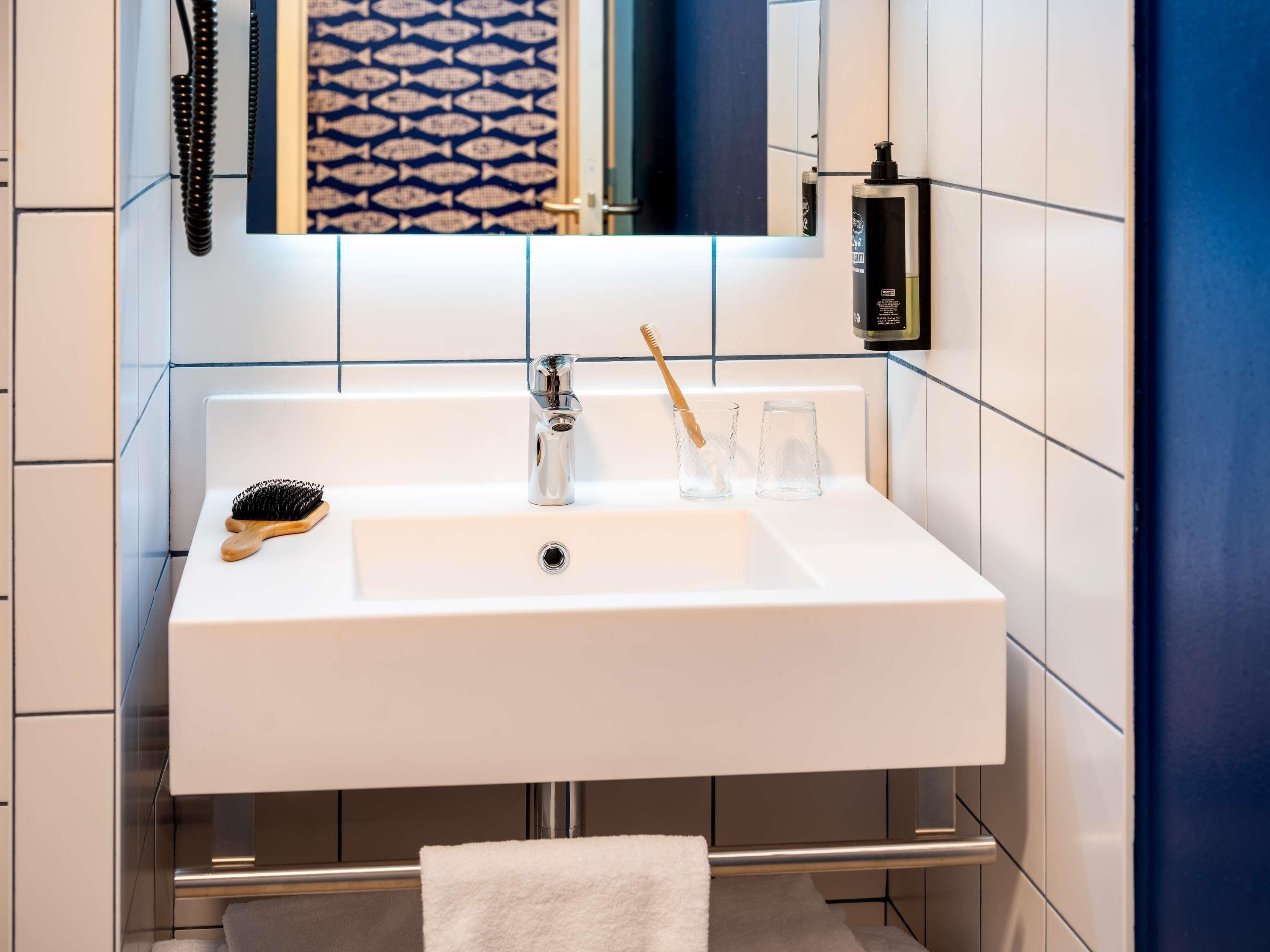 Un baño con un lavabo blanco, un espejo, un perchero para toallas y un portacepillos.