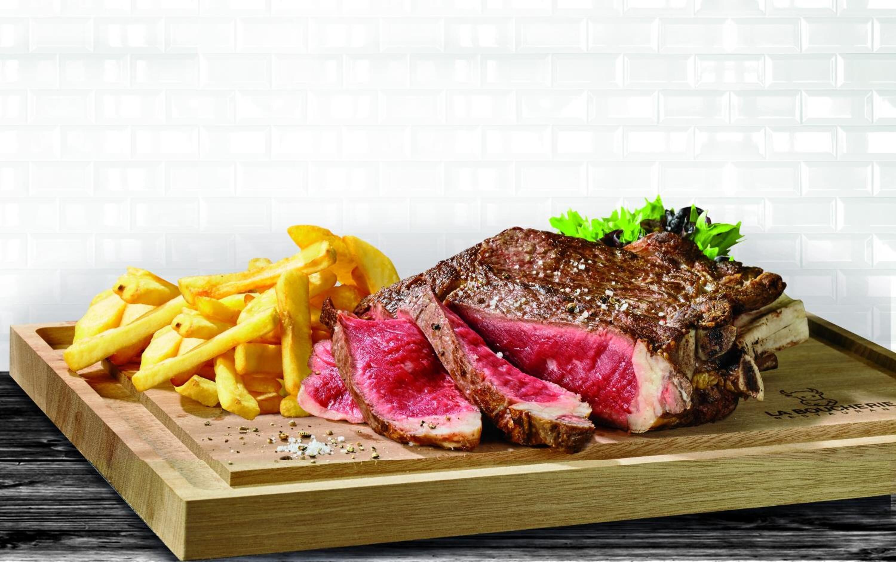 Een houten dienblad met een steak, frieten en garnering.