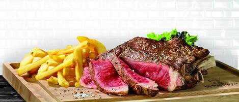 Una bandeja de madera con un bistec, papas fritas y una guarnición.